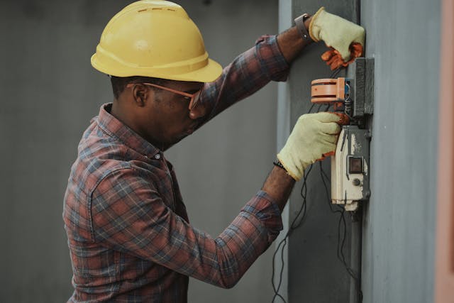 Person wearing a hard hat, glasses and gloves inspecting wiring